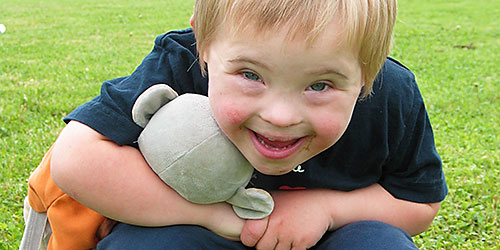 un petit garçon accroupi dans l'herbe avec son doudou