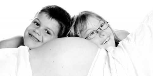 Une fillette et un garçonnet sourient, leurs têtes posées sur le ventre de leur maman enceinte.